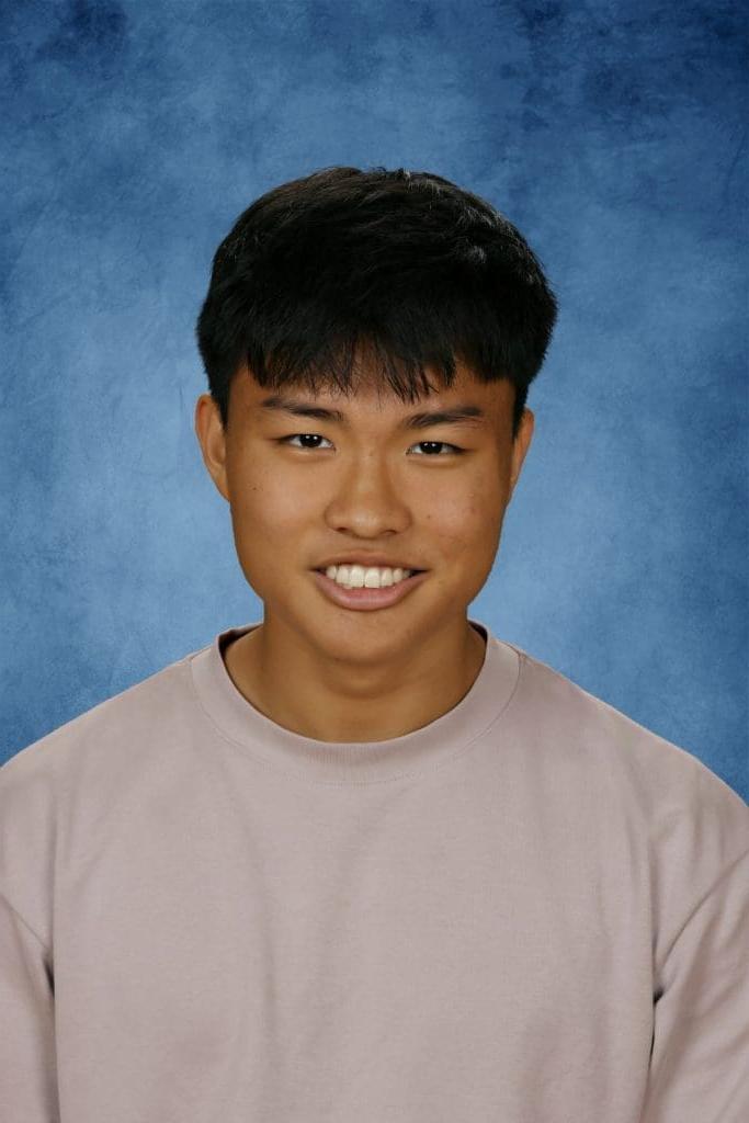 Young man smiling, blue background, casual attire.